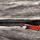 Фотопанно All you need is red, Mr Perswall с изображением ярко-красной лодки на фоне черно-белой речной глади, в которой отражается затянутое облаками небо и лесистые холмы. Выбрать, заказать фотообои для стен в салонах ОДизайн, печать по индивидуальным размерам.