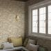 Интерьер зоны отдыха с флизелиновыми обоями Boråstapeter Alnarp Beige (арт. 8716). Пышный пейзажный узор с деревьями, рекой и мостом в тёплой бежевой палитре. Уютная усадебная обстановка с лавкой, подушками, окном и латунным бра. Коллекция Herrgård от Boråstapeter.